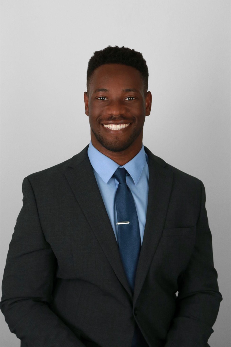Corporate headshot example: a professional in formal dark business attire against a neutral studio background